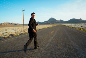 Businessman running down desert road, looking back
